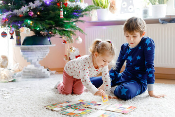 Two little chilren, cute toddler girl and school kid boy playing together card game by decorated...