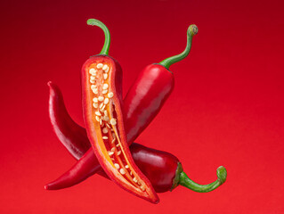 Fresh red chilli peppers and cross sections of chilli pepper with seeds floating in the air.