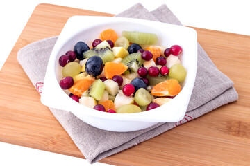 Fresh fruit salad with sliced kiwi, tangerine, apples, grapes and cranberries in a white bowl. 