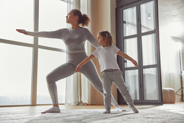 Fototapeta na wymiar Low angle of calm mother doing asana while little girl is assisting her in living room