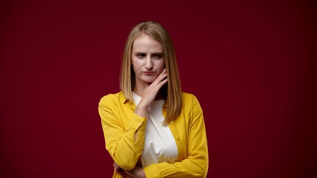 the girl stands and thinks, but the idea never occurs to her, she does not know what to do, she is dressed in a yellow shirt and a white T-shirt, the background is red