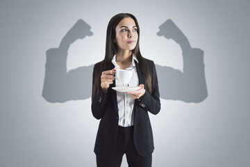 Portrait of attractive young european businesswoman with coffee cup and shadow muscle arms on...