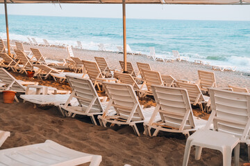 Empty Sun loungers in front of sea. Sun chairs on sandy beach. Big waves stormy weather. An empty...