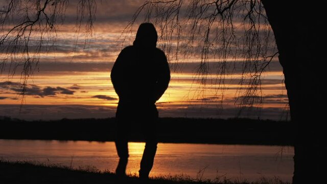 The silhouette of a man walks along the river bank during sunset.