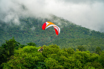 The sportsman on a paramotor gliding and flying in the air with majestic clouds and green forest...