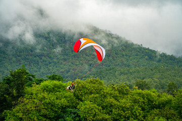 The sportsman on a paramotor gliding and flying in the air with majestic clouds and green forest are background. Paramotor it is extreme sport.