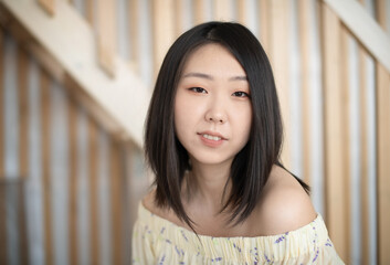 Portrait of a beautiful Asian young woman in a white trendy shirt at home in a light loft interior.