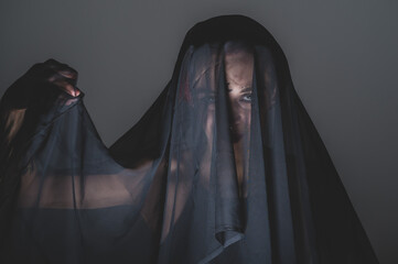 Redhead woman with a black veil on her head in a dark studio. A girl with an earring in her nose...