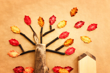 Concept image of handmade wooden tree and autumn leaves on brown recycled paper background