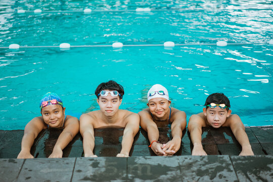 four asian teenagers in swimsuits smiling at camera while resting by the pool