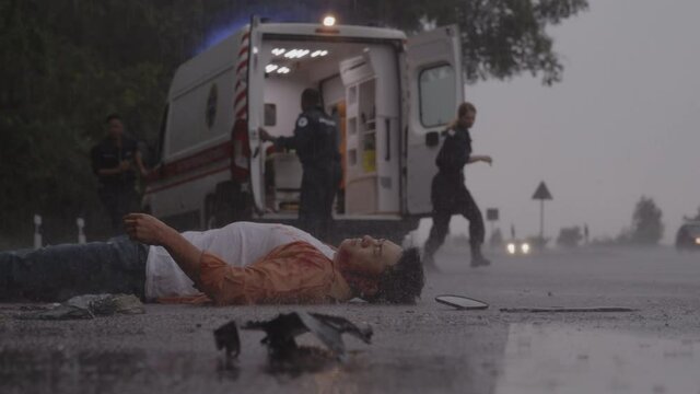 Team of paramedics helping man lying on road under rain