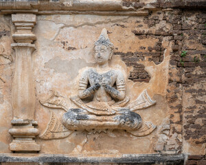 Beautiful ancient stucco life size carving of sitting deity on wall of Wat Chet Yot or Wat Jed Yod buddhist temple, historic landmark of Chiang Mai, Thailand