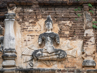 Fototapeta na wymiar Beautiful ancient stucco life size carving of sitting deity on wall of Wat Chet Yot or Wat Jed Yod buddhist temple, historic landmark of Chiang Mai, Thailand