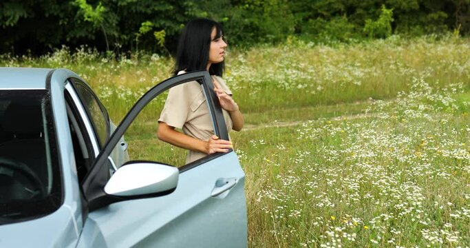 Woman gets out of the car ooking around and walking on the flowers field, meadow in countryside during journey, travel, feel the nature, alone trip, relax.