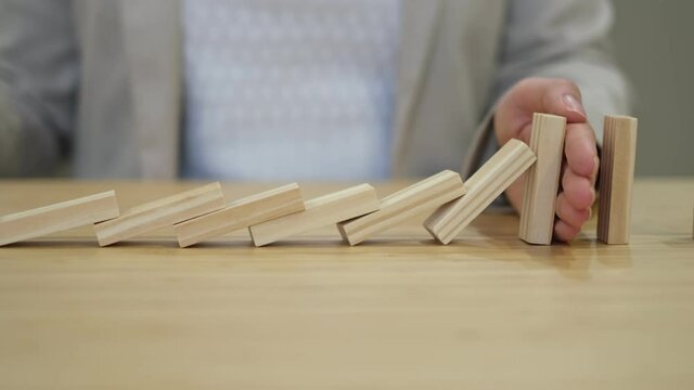 businessperson hand stopping colorful blocks from falling on table in office. domino effect in business.