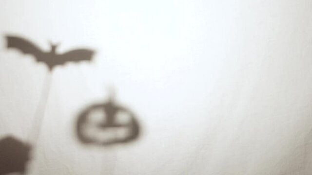 Halloween vampire bat and pumpkin shadow puppets silhouetted on sticks behind a white sheet
