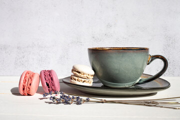 Ceramic cup with tea , colorful fresh macaroons and a bouquet of dried lavender on a gray background. View from the side, space for text. Beautiful table setting.