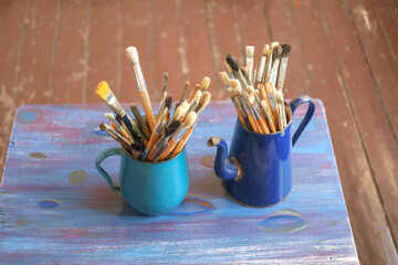 Various professional paint brushes in the blue metal jars on the table, selective focus