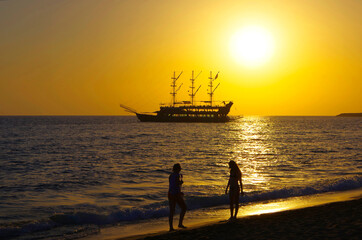 Silhouette of an excursion pleasure ship and people on the Mediterranean coast against the backdrop of the setting sun. Turkey city of Alanya.