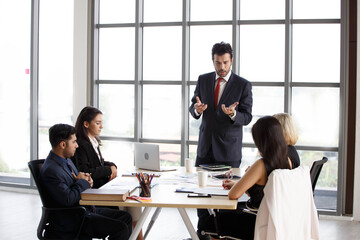 latin executive leader discussion with colleague in meeting with data in laptop computer on window in office . adult businessman manager talking and advise to coworkers in conference . boss training.