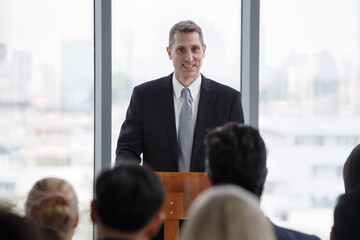 senior businessman standing at podium giving a speech addressing a conference in seminar. old...