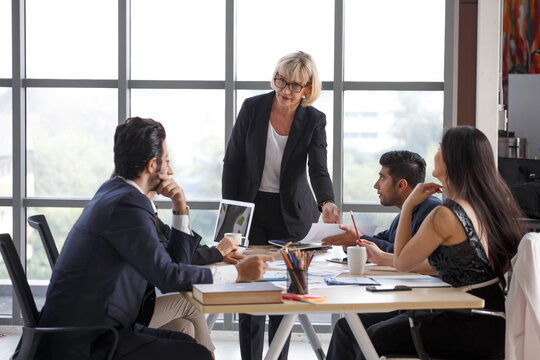 senior executive leader female discussion with colleague in meeting with data in laptop computer on window in office . old businesswoman manager talking and advise to coworkers in conference .. - Powered by Adobe