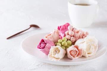 Sweet roses from marshmallows on a plate with a cup of green tea.