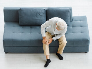 Caucasian old senior elderly unhealthy sick illness gray hair man sitting on sofa in living room at...