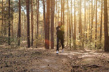 Obraz premium Young athletic woman jogging in forest in sunny morning. Healthy lifestyle concept.