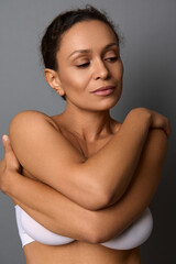 Fototapeta na wymiar Close-up beauty portrait of self-confident middle aged African woman with perfect clean shiny healthy skin, hugging herself, isolated over gray background with copy space. Body and skin care concept