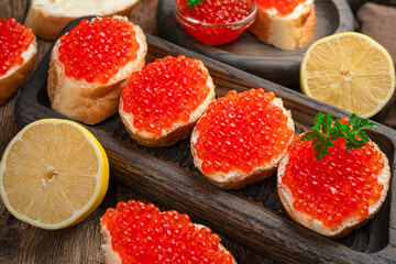 Fototapeta na wymiar Sandwiches with red caviar, butter, parsley and lemon on a wooden background.