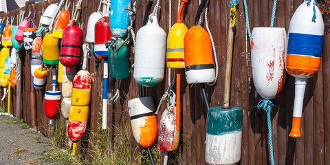 A brown wooden fence decorated with old lobster floats in the Atlantic Ocean as a symbol of the fishing village