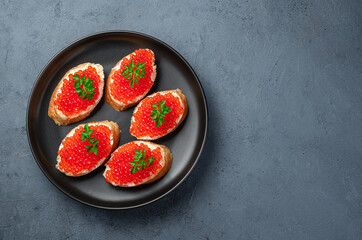 Sandwiches with red caviar in a black plate on a dark blue background.