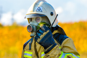 A close-up firefighter rescuer in a protective suit, gas mask and white helmet extinguishes a...
