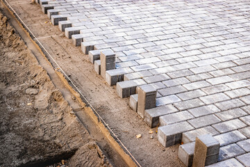 Pavement repairs and paving slabs laying on the prepared surface, with tile cubes in the background. Laying paving slabs in the pedestrian zone of the city. Paving slabs and curbs.