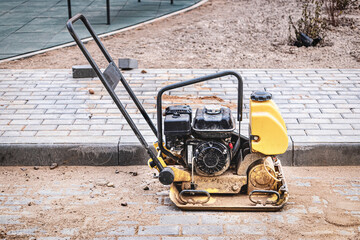 Vibratory rammer with vibrating plate on a construction site. Compaction of the soil before laying paving slabs. Close-up.