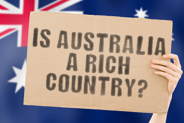 The question " Is Australia a rich country? " on a banner in men's hand. Money. Finance. Currency. Rate. Economy. Wealth. Salary. GDP. Million. Inequality. Economic. Income