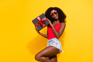 Photo of optimistic nice brunette lady hold present wear eyewear top shorts isolated on yellow color background