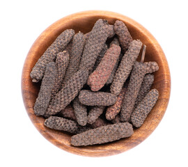 Long pepper in wooden bowl, isolated on white background. Heap of pippali or piper longum. Top view. - obrazy, fototapety, plakaty