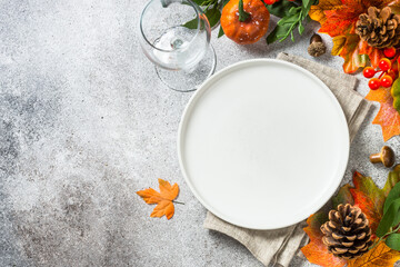 Autumn table setting with white plate, candles and fall decorations with pumpkins at kitchen table. Top view with copy space.