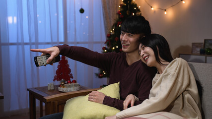 happy couple talking watching tv on Christmas holiday at home. joyful man and woman relax on couch...
