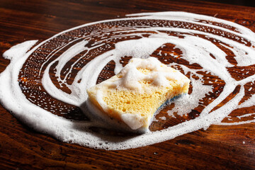 cleaning sponge wiping foam soap suds on wooden background, household washing concept