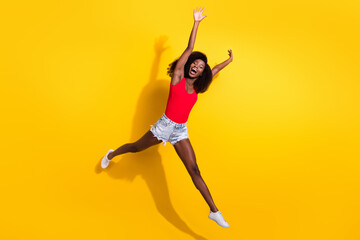Fototapeta na wymiar Full length photo of cheerful afro american lady jump up raise hands good mood isolated on yellow color background