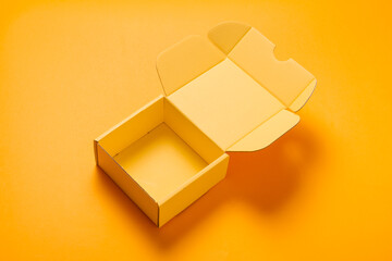 Simple yellow cardboard box on color background, opened, empty inside
