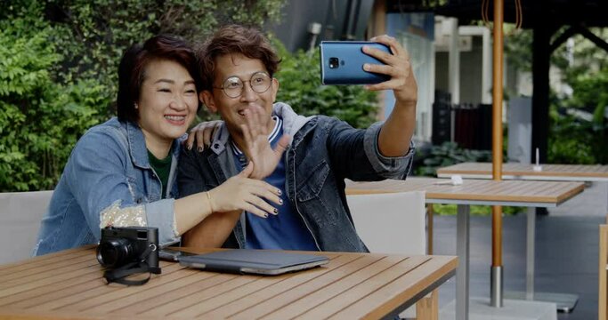 Family Asian couples using smartphones to take selfies on their summer garden vacation. Sit and chat on video call with happy smile in park. Leisure activities after opening city to live independent