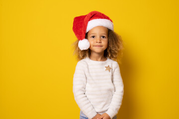 Cute little girl in santa claus hat isolated over yellow background.