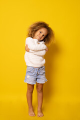 Portrait of charming little girl embracing herself isolated over yellow background.