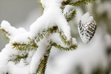 A shiny silver color Christmas ornament hanging from a pine tree with snow