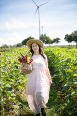 Smiling white young woman with long hair in light dress in the countryside in straw hat with flowers in her hands