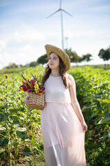 White young woman with long hair in light dress in the countryside in straw hat with flowers in her hands